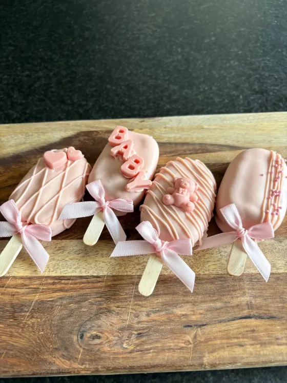 Roze gedipte cakepops op een stokje, versierd met strikjes