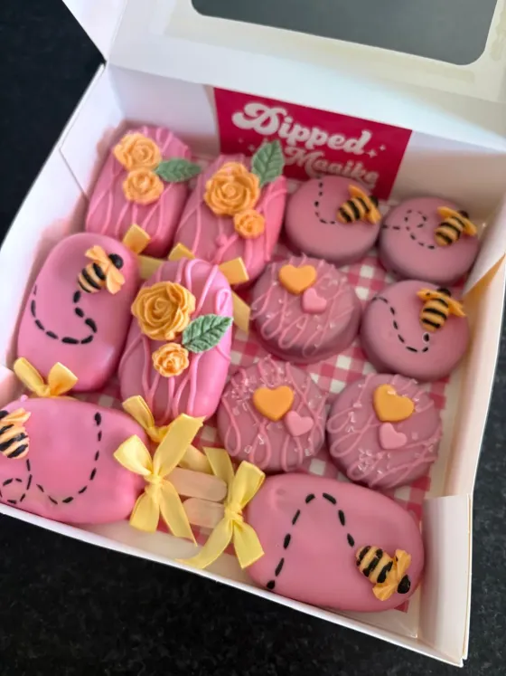 Roze gedipte koekjes met bijen en bloemenversiering in een cadeaubox met Dipped by Maaike-logo
