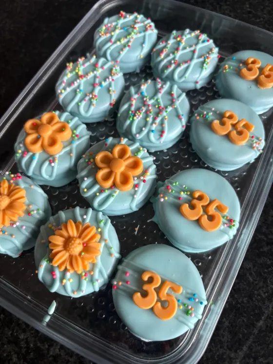 Turquoise gedipte koekjes met oranje bloemen en het cijfer 35, verjaardagsthema